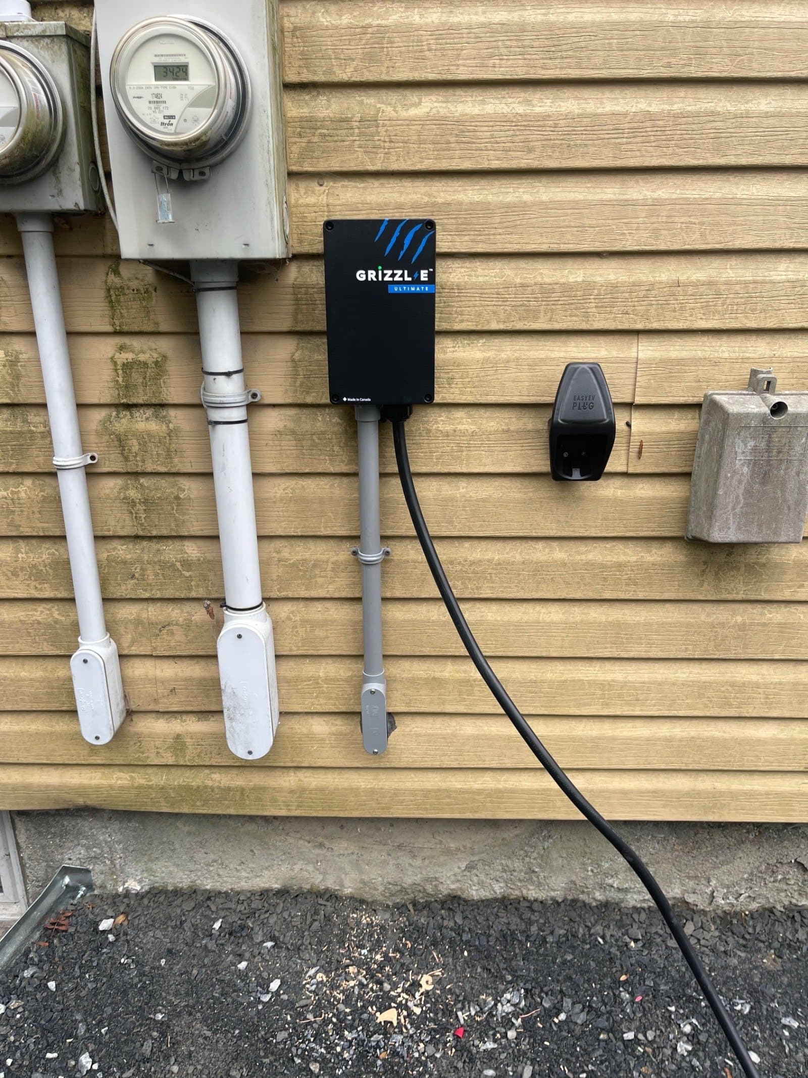 Black Grizzl-E charger installed next to a building’s meters, grey conduit along the wall